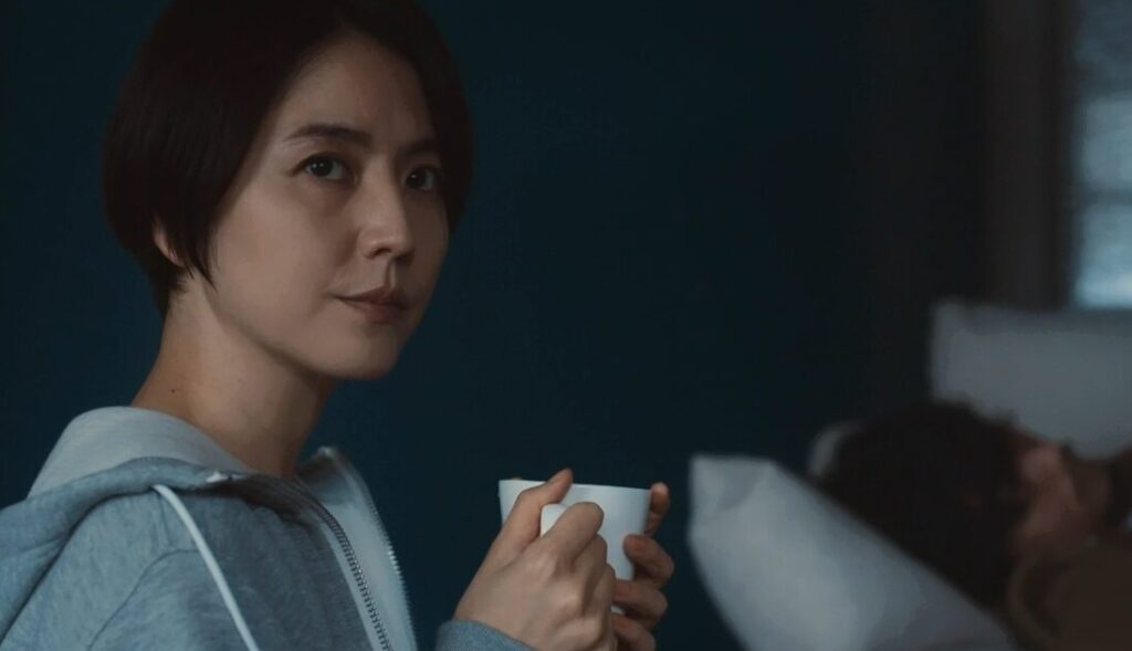 ドラマ「エルピス―希望、あるいは災い―」第５話、自宅のソファで寝る岸本拓朗（眞栄田郷敦）の横で、コーヒーを飲みながら窓の外を見る浅川恵那（長澤まさみ）