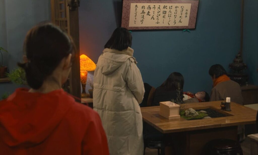 ドラマ「妻、小学生になる。」第８話、お店の中で眠っている白石万理華（毎田暖乃）を見守っている新島圭介(堤真一)たちを見ている新島貴恵（石田ゆり子)