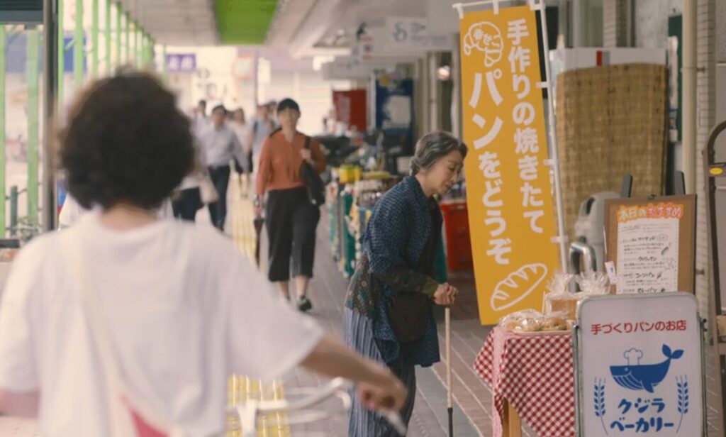 ドラマ「凪のお暇」第1話、『エレガンスパレス』ちかくの商店街『くじらロード』のパン屋で、パンの耳をもらう吉永緑(三田佳子)